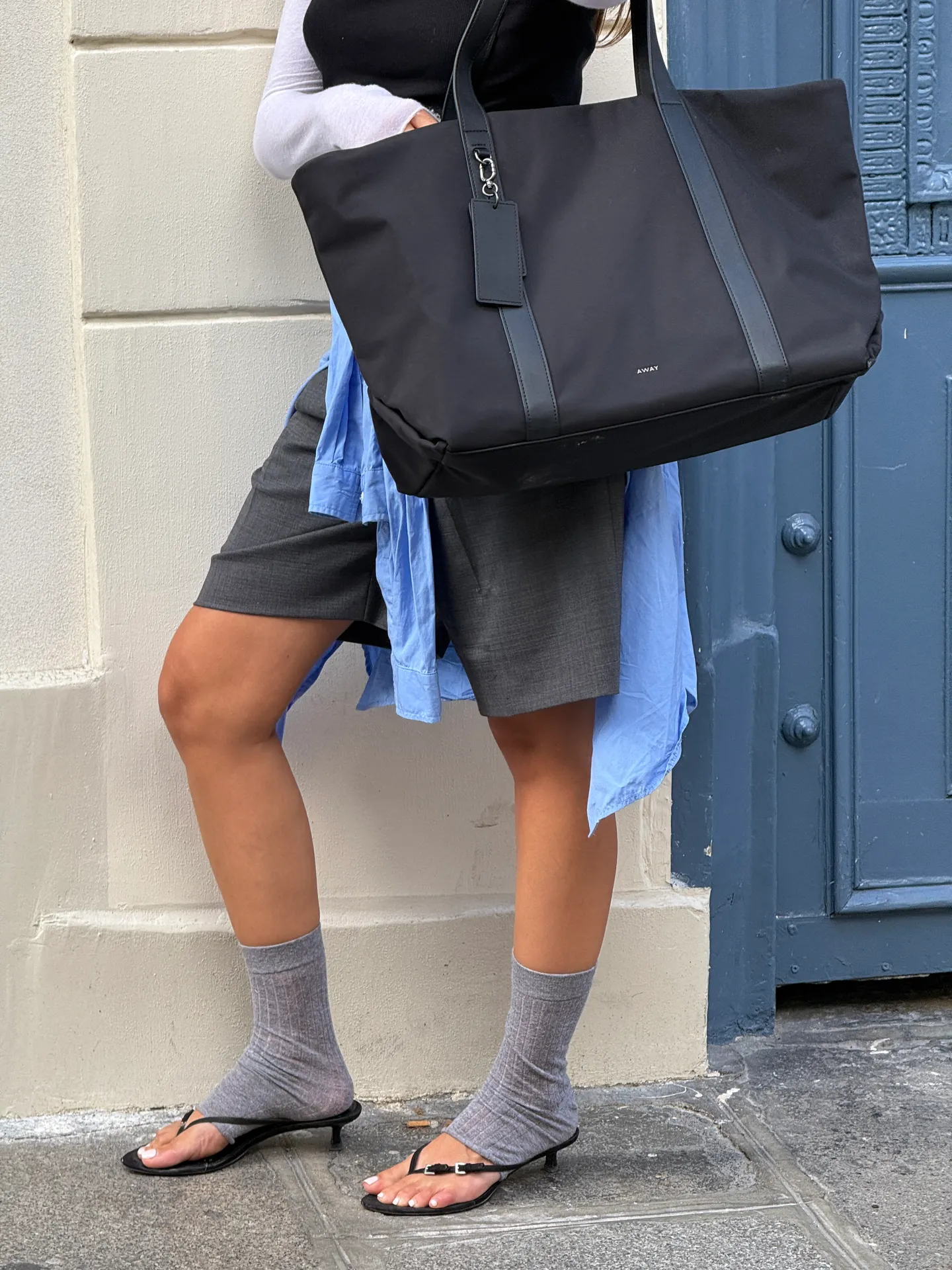 Black tank top over white long-sleeve, gray shorts, blue shirt, gray socks, black flip-flop heels, and a black tote bag.