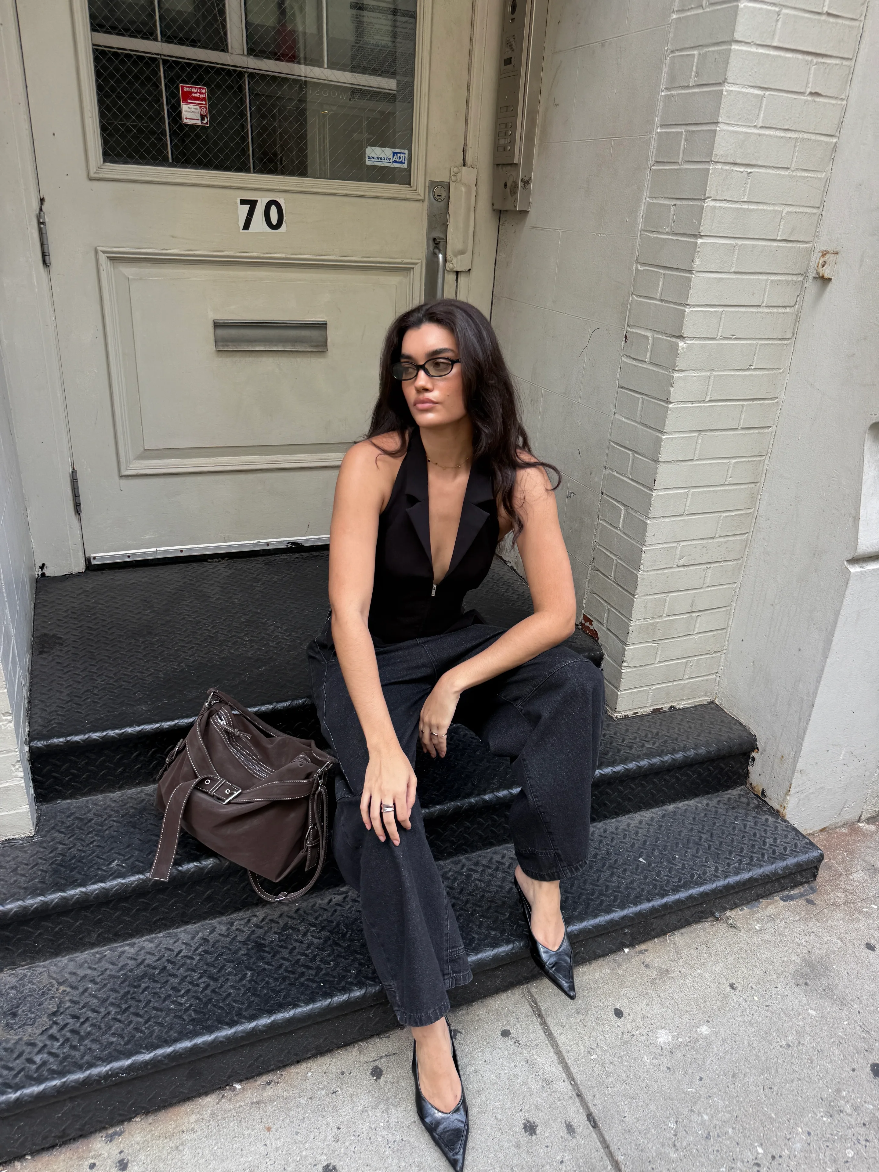 Black halter top, dark jeans, and pointed black mules on metal stairs.