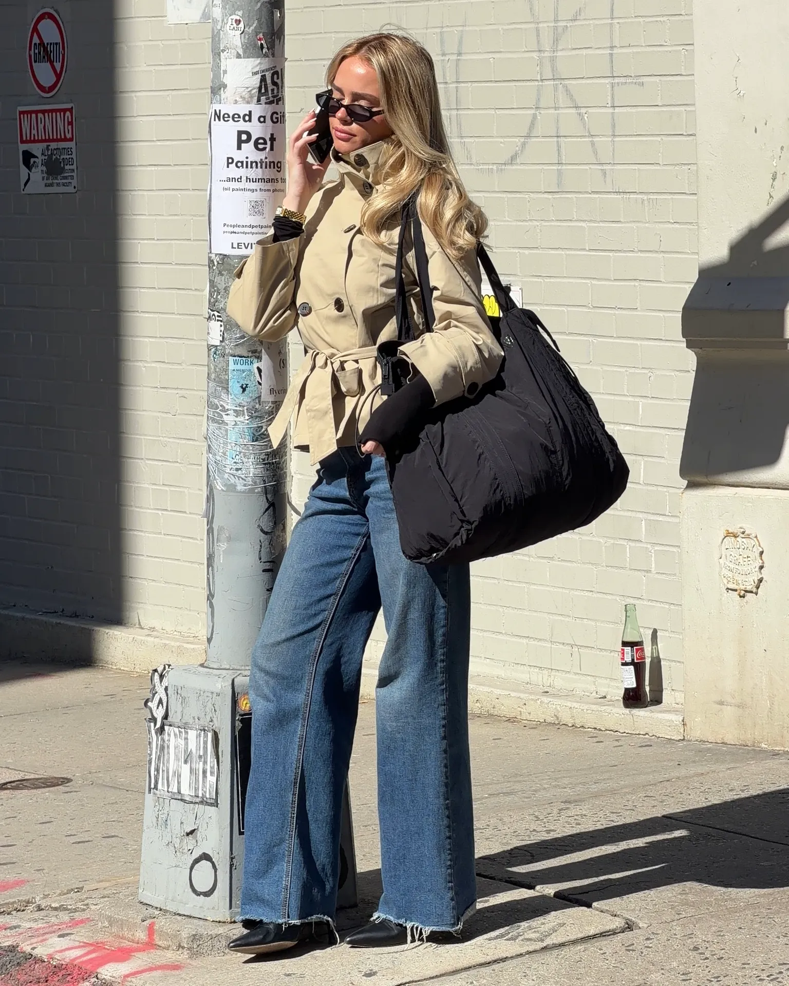 Khaki trench coat, wide-leg jeans, black top, and black tote bag street style.