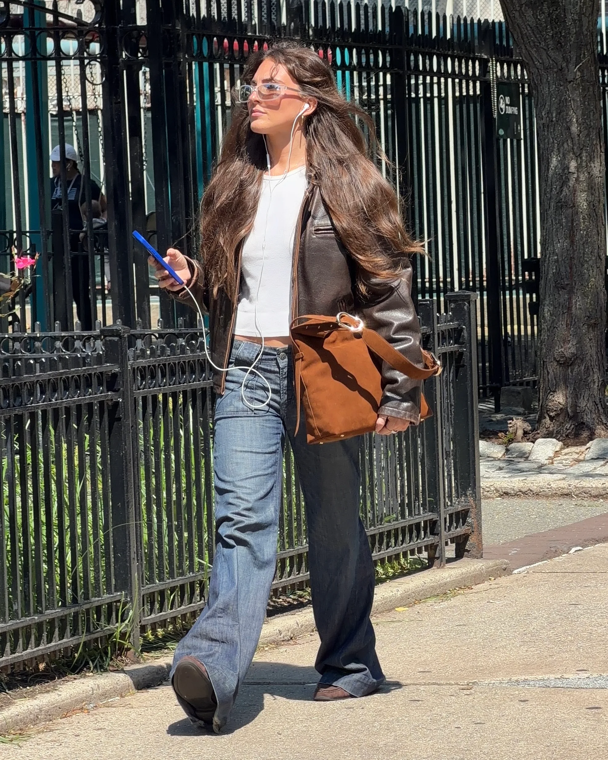 Brown leather jacket, white top, flared jeans, and brown tote bag on a sunny street.