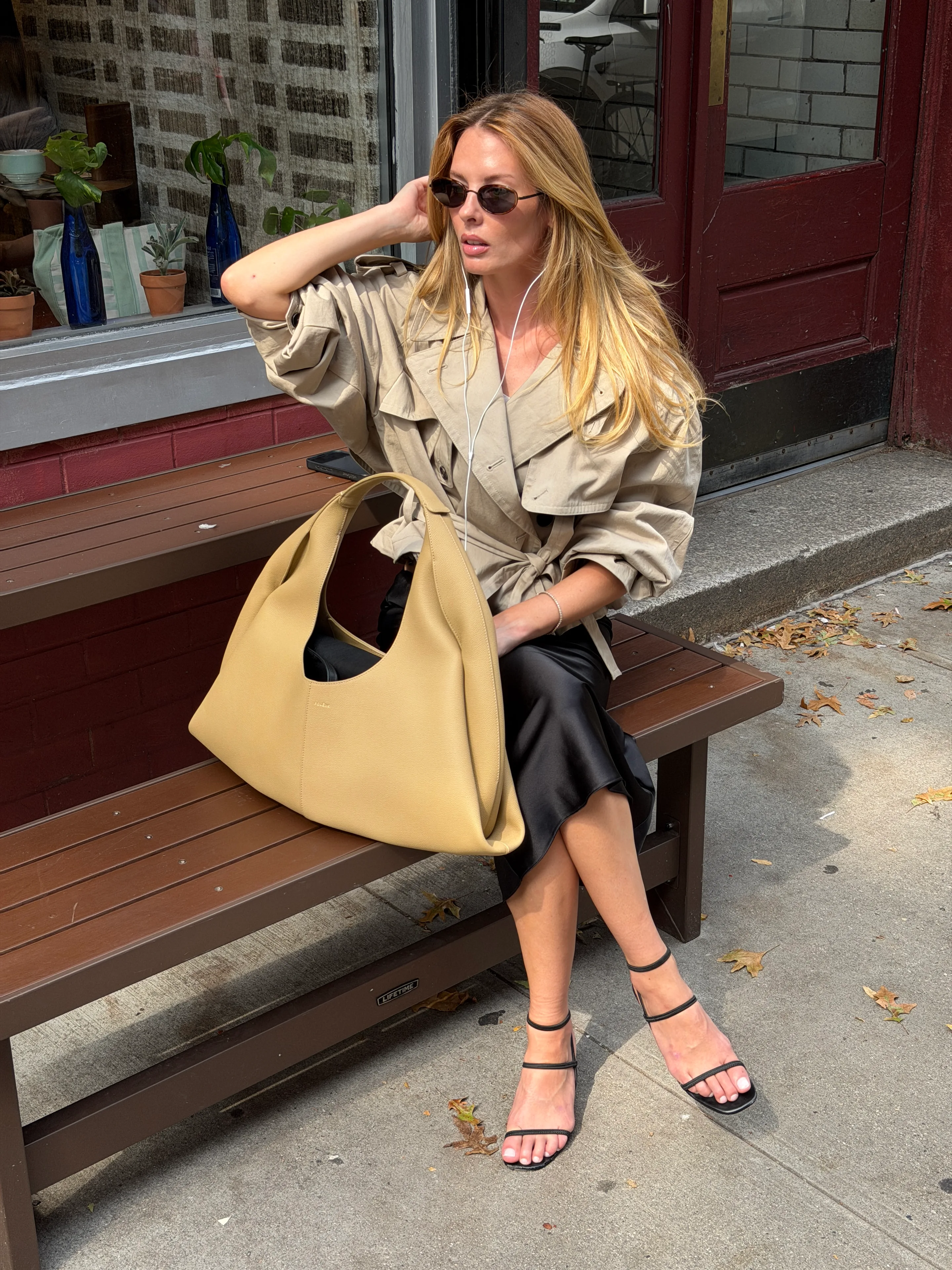 Beige trench coat with black slip skirt, black sandals, and a large beige bag.