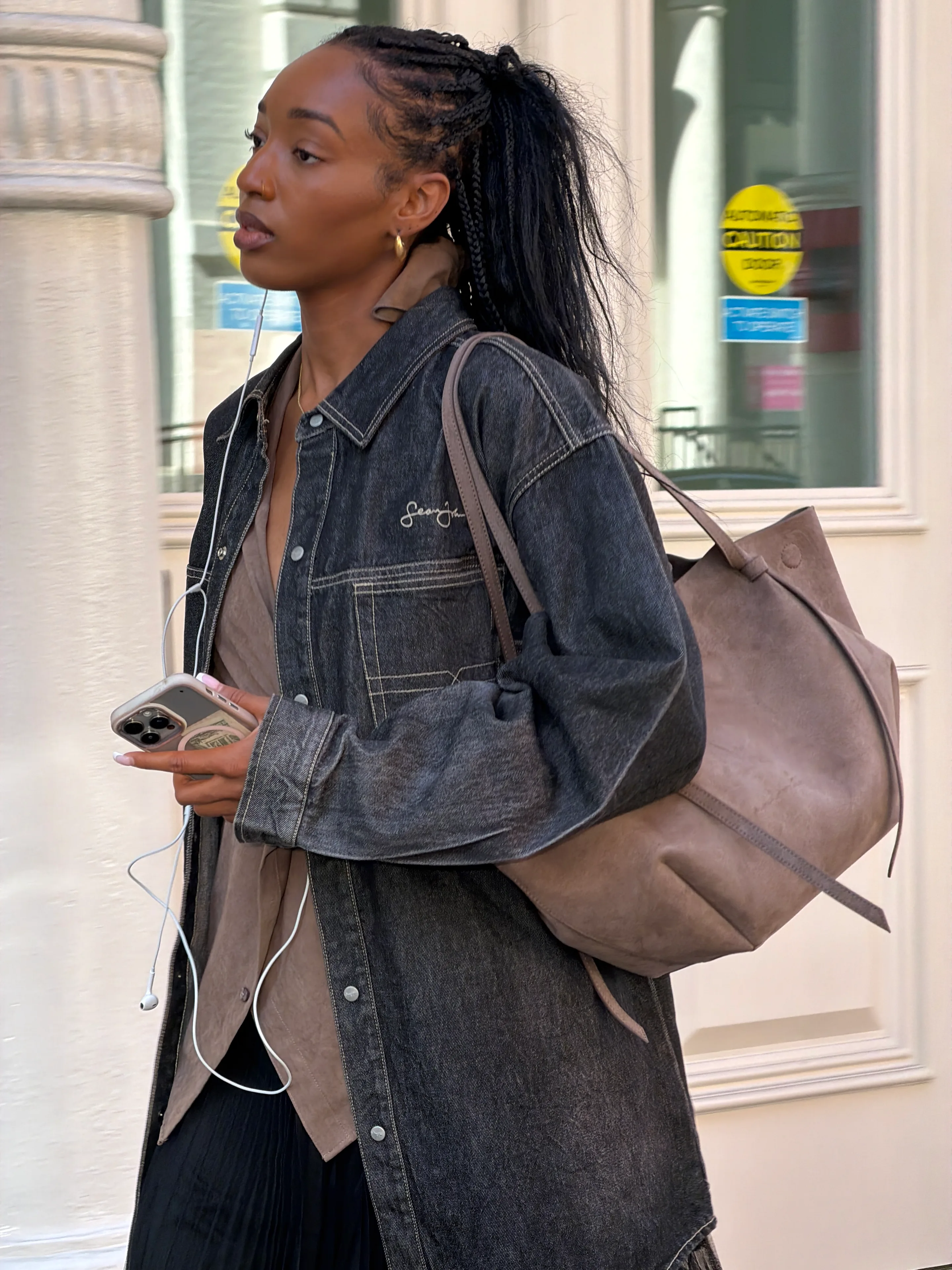 Dark denim jacket over a tan shirt, black skirt, and taupe shoulder bag.