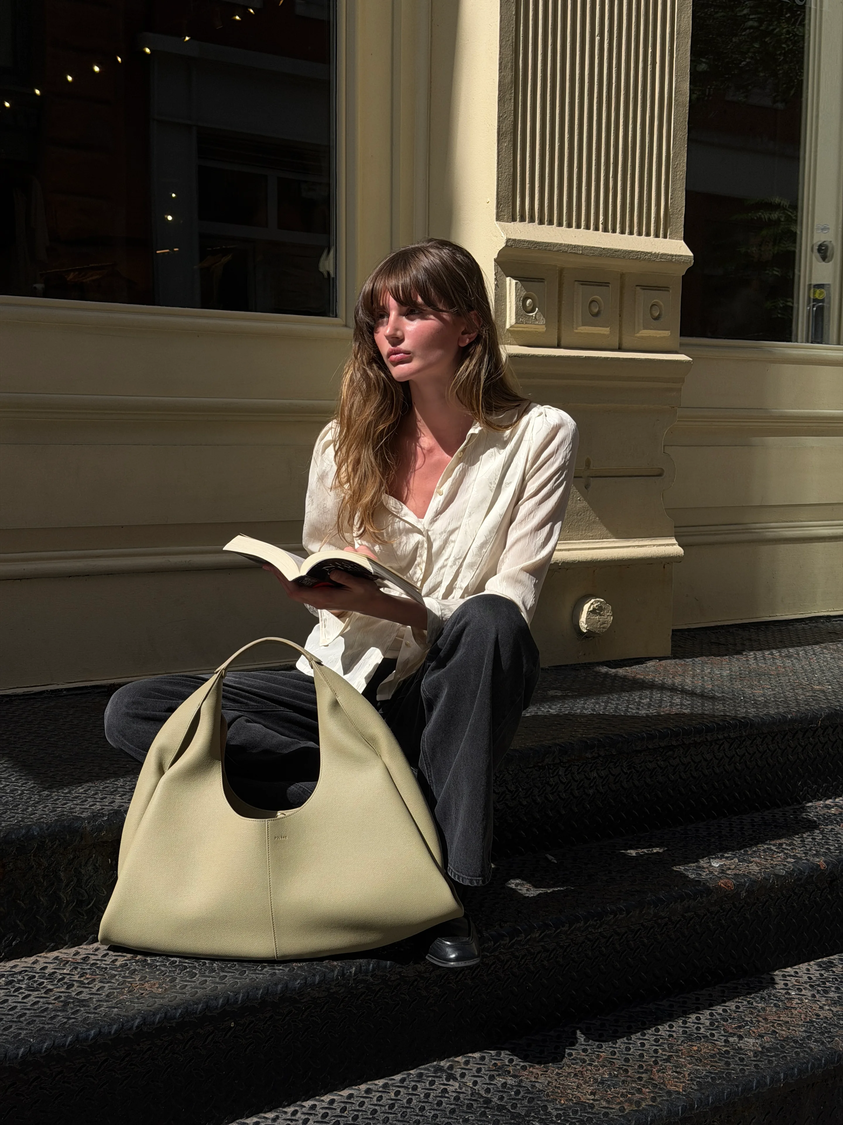White button-down shirt, dark jeans, and olive handbag on metal steps in sunlight.