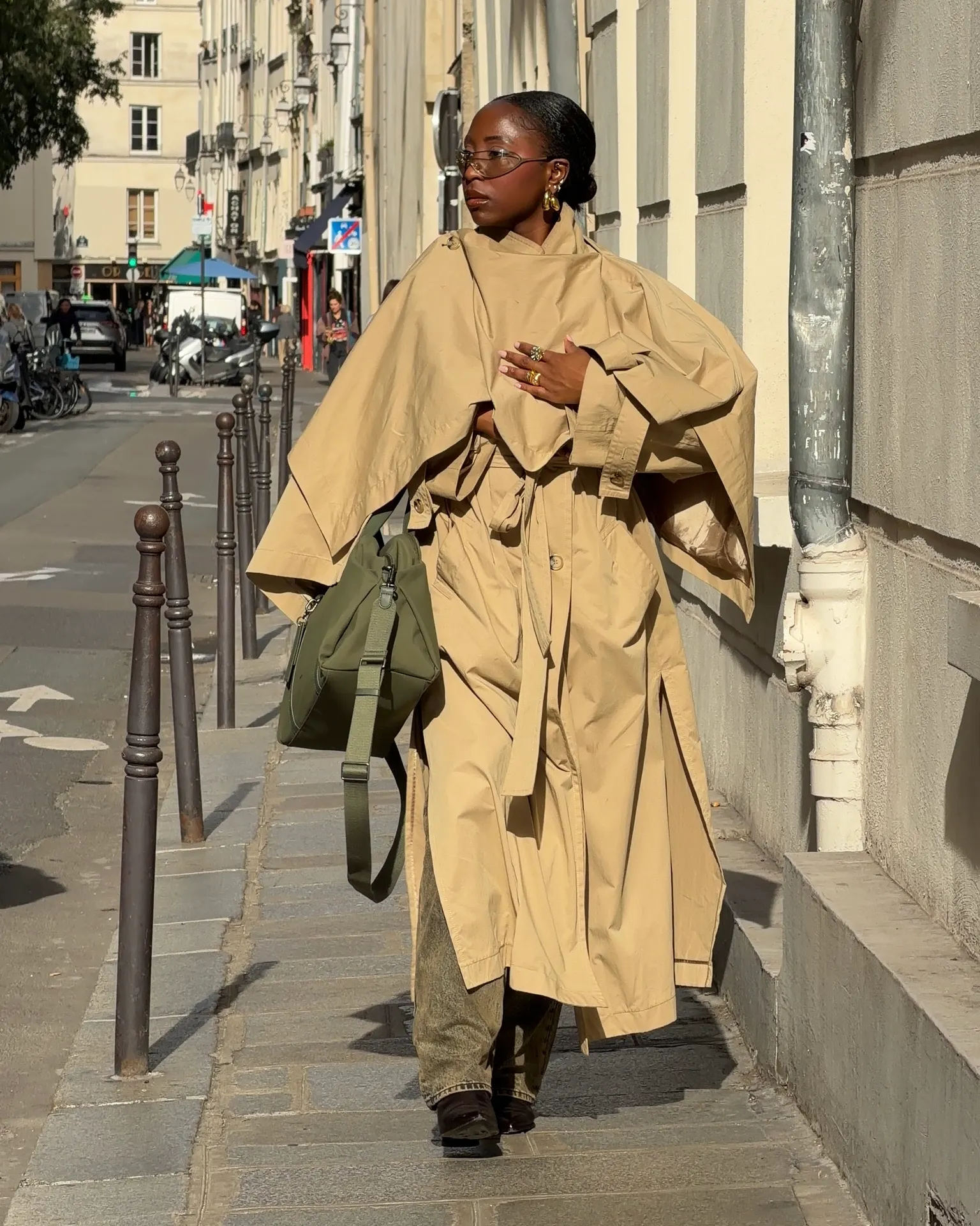 Oversized khaki trench coat, green shoulder bag, gold jewelry, and glasses on a city street.