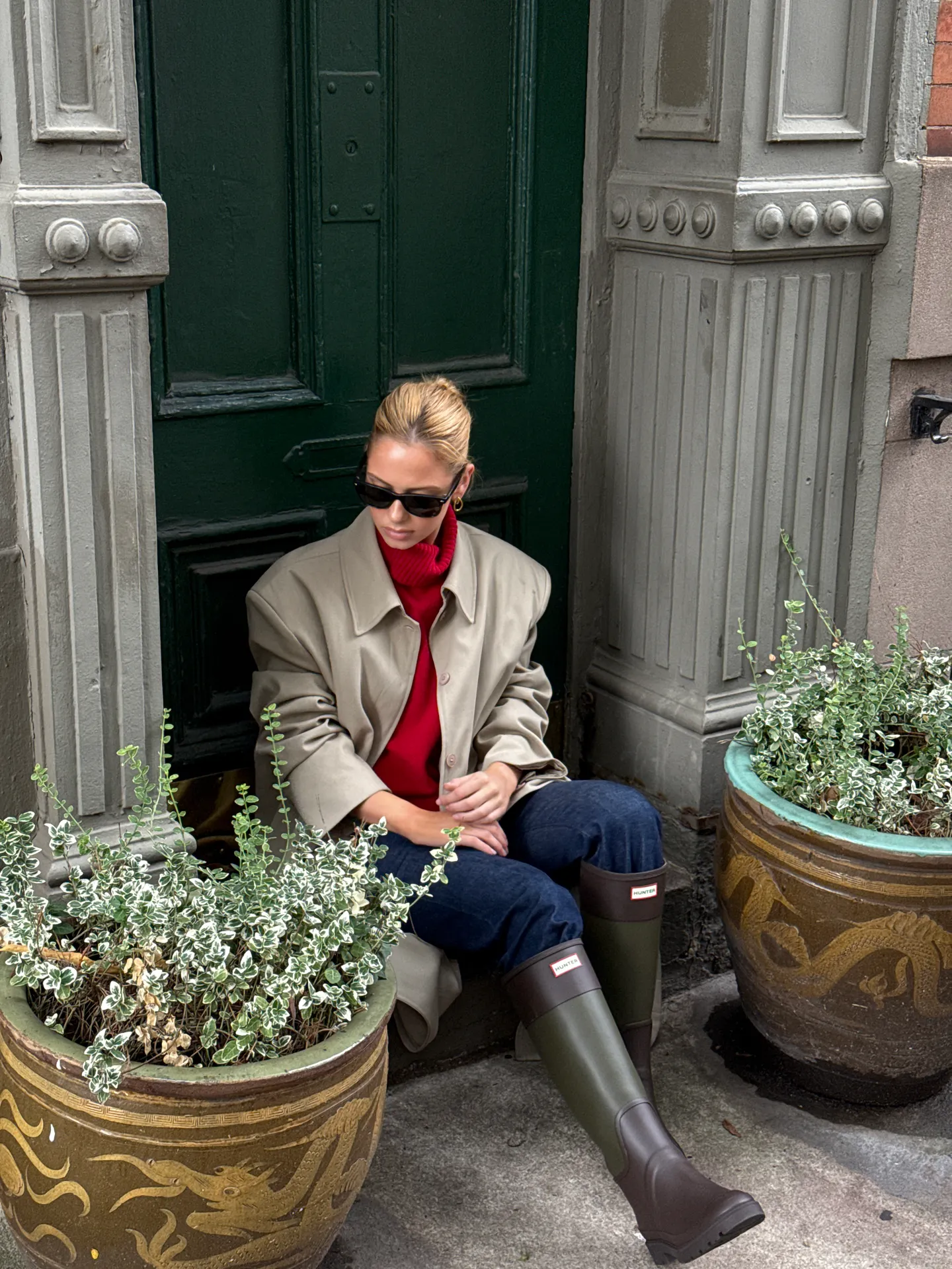 Red turtleneck, beige jacket, blue jeans, and olive green Hunter rain boots.