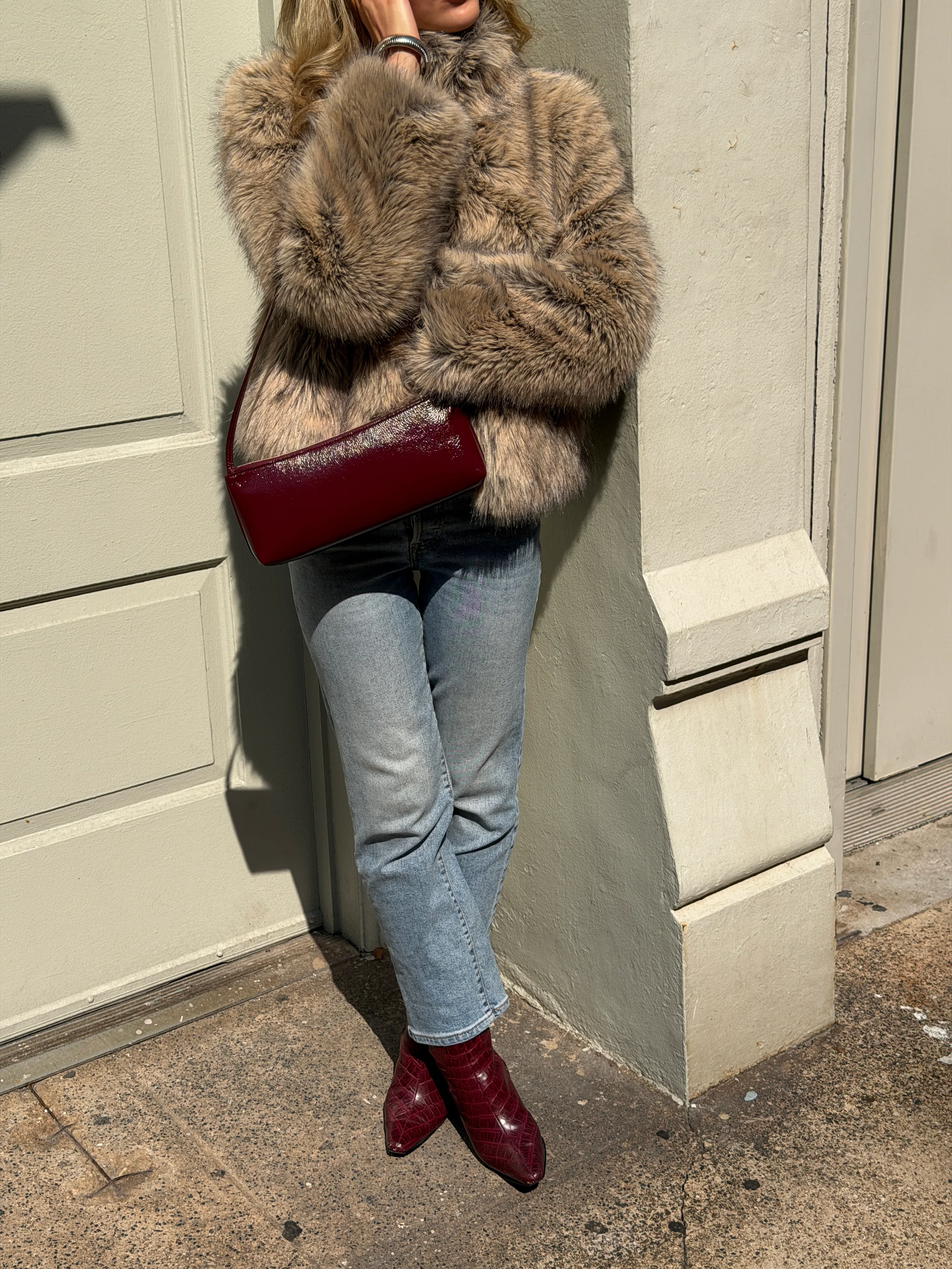 Brown faux fur coat with a red patent leather bag, light wash jeans, and red croc-embossed boots.