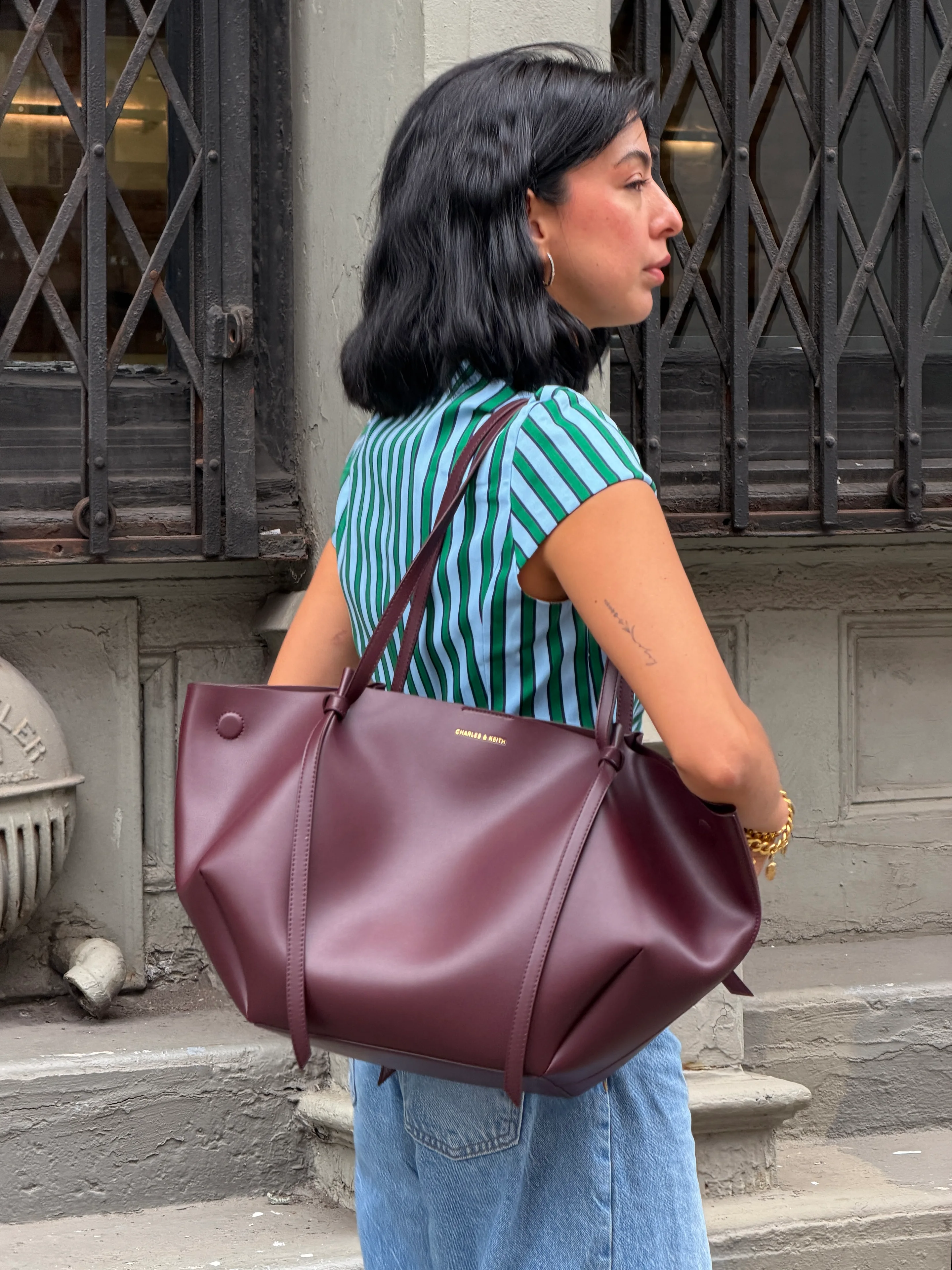 Green and blue striped top, blue jeans, and a burgundy tote bag.
