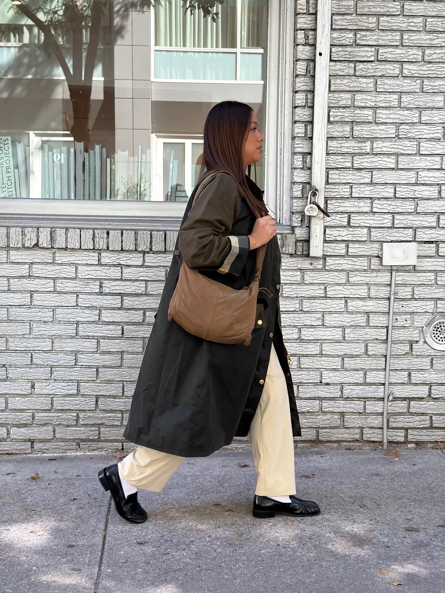Long olive coat over cream pants and black loafers, brown shoulder bag.