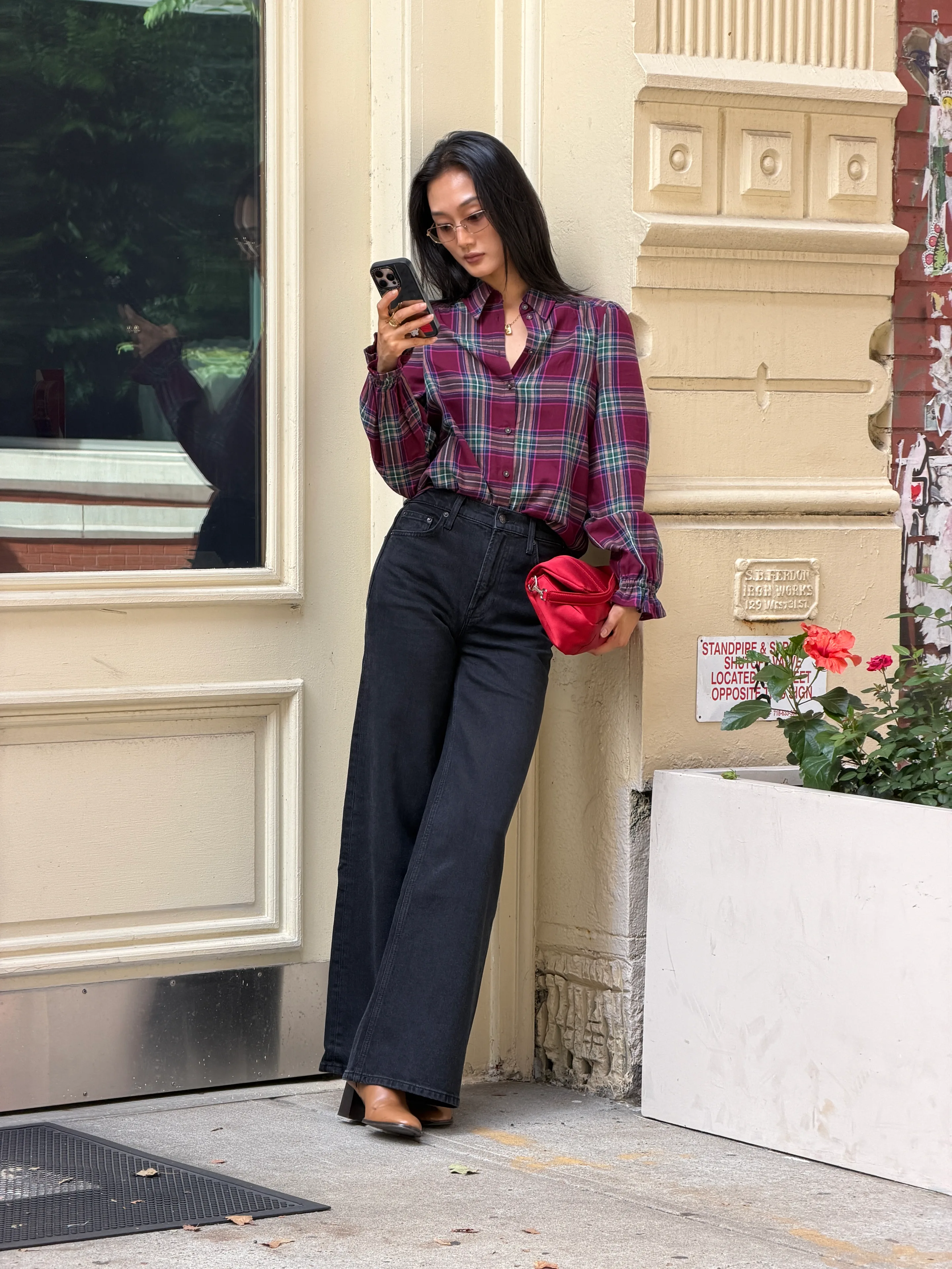 Maroon plaid shirt, dark wash wide-leg jeans, and tan mules, accessorized with a red bag.