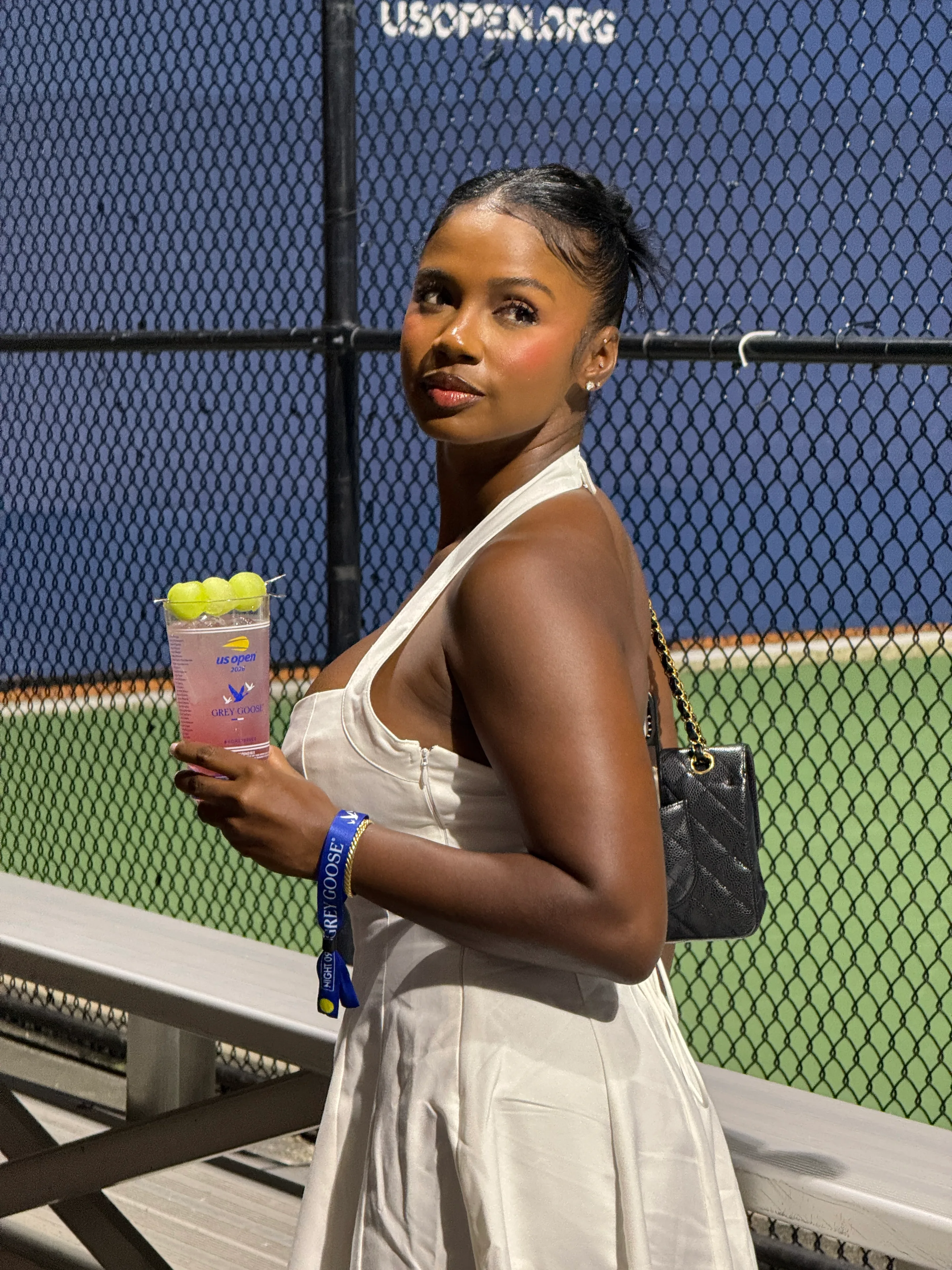 White halter dress at US Open, holding cocktail with grapes.