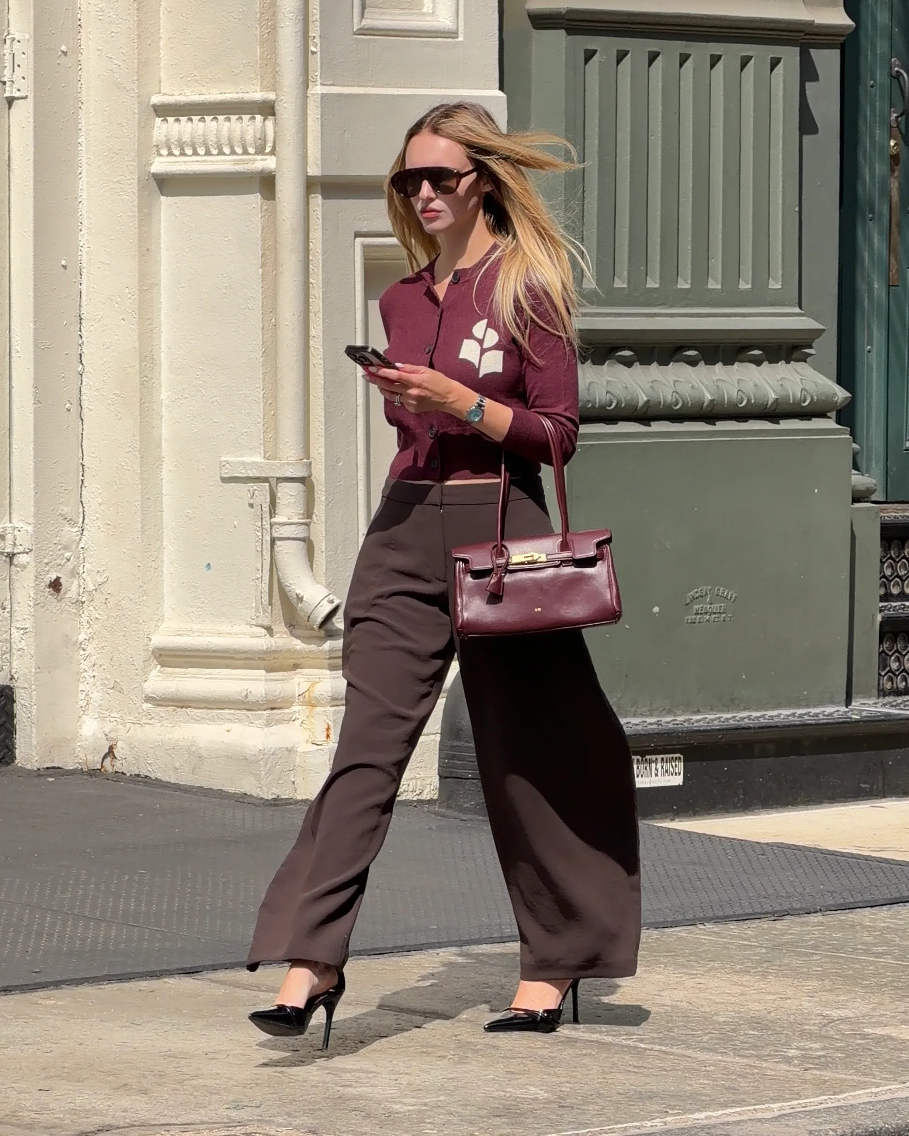 Burgundy cropped cardigan with white logo, brown wide-leg pants, black heels, and burgundy bag.