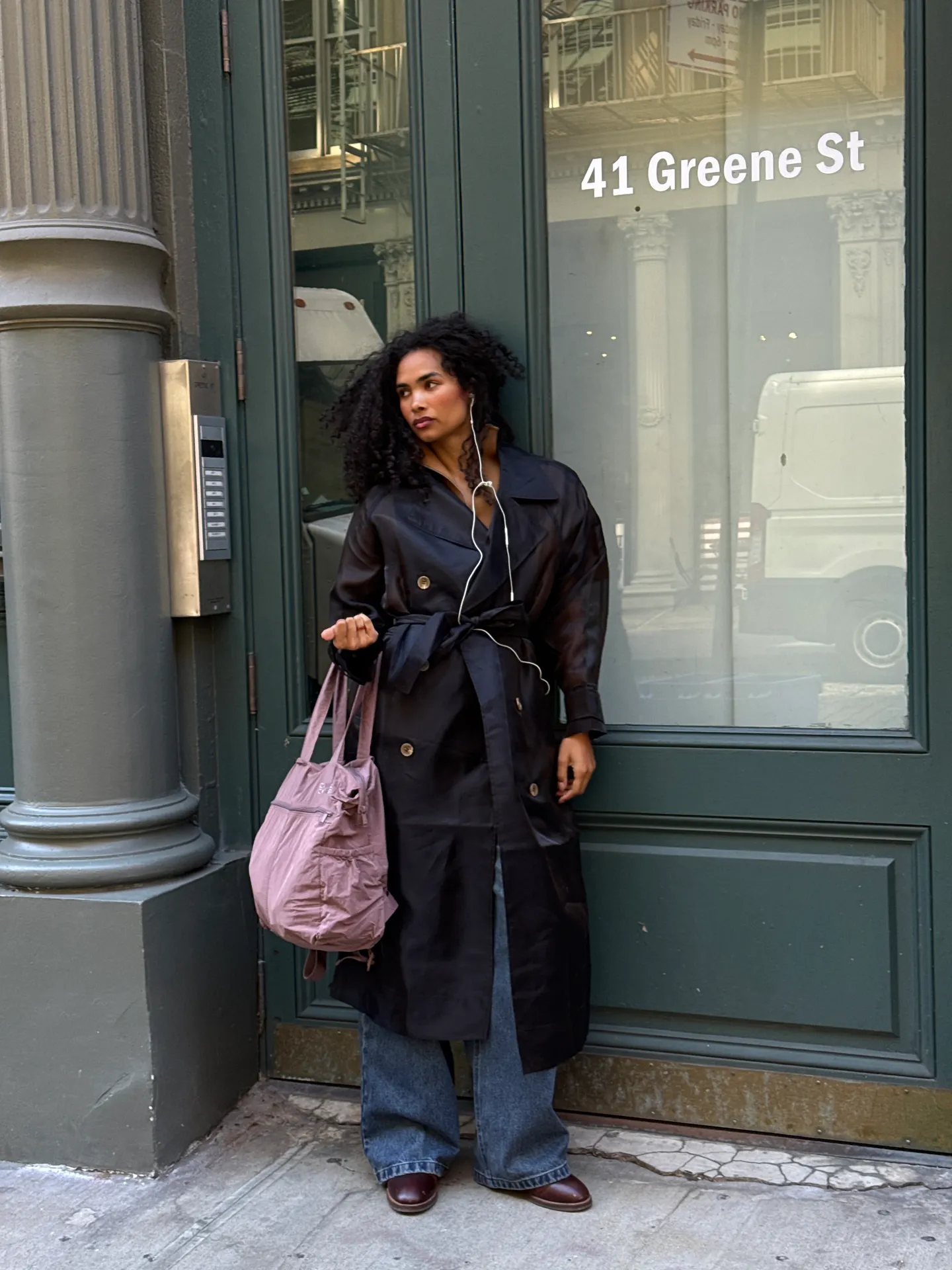 Black belted trench coat with wide-leg jeans, burgundy shoes, and pink tote bag.