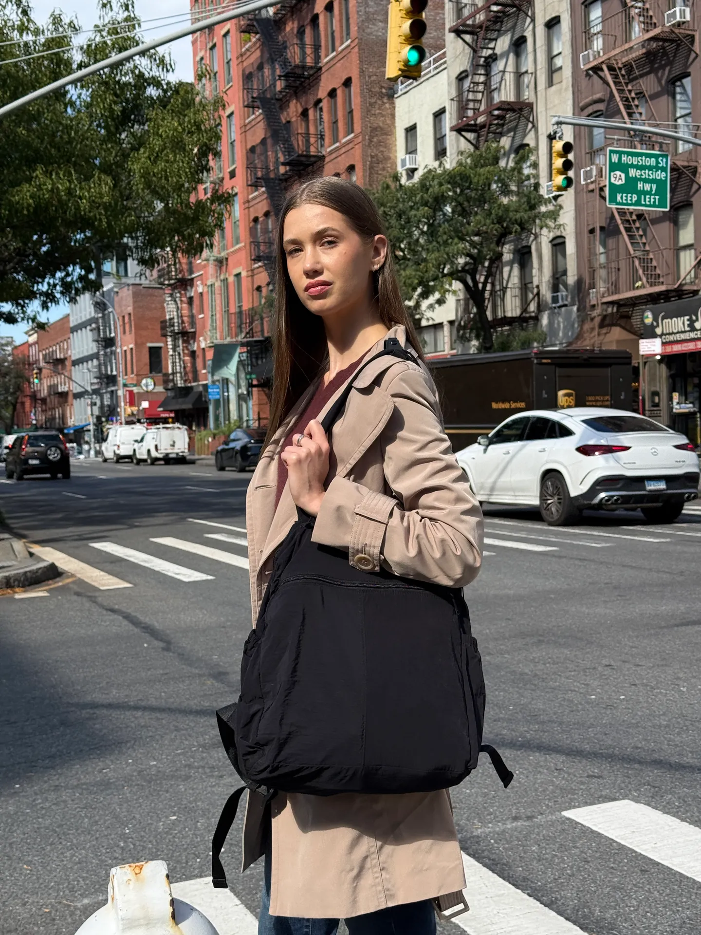 Tan trench coat over burgundy top and black backpack on a city street.