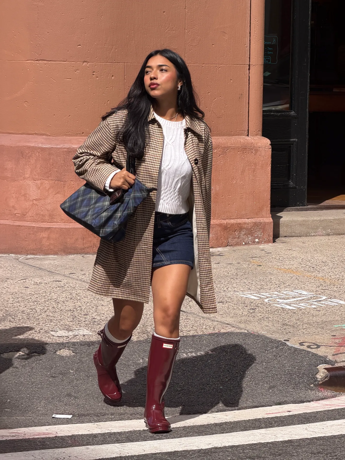 Houndstooth coat, white cable-knit sweater, denim skirt, Hunter boots, and plaid tote bag.