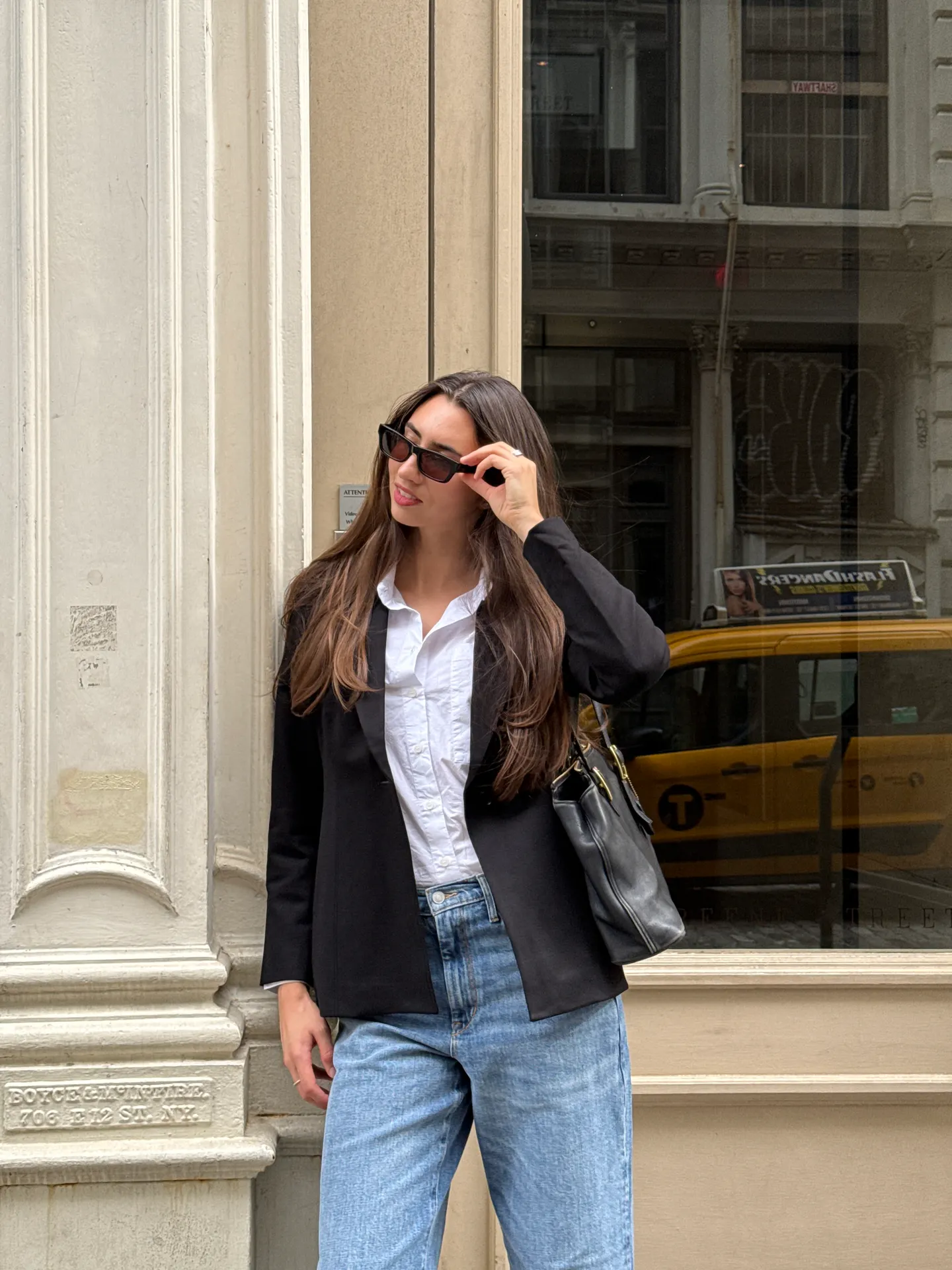 Black blazer, white shirt, light wash jeans, and black sunglasses with a leather bag.