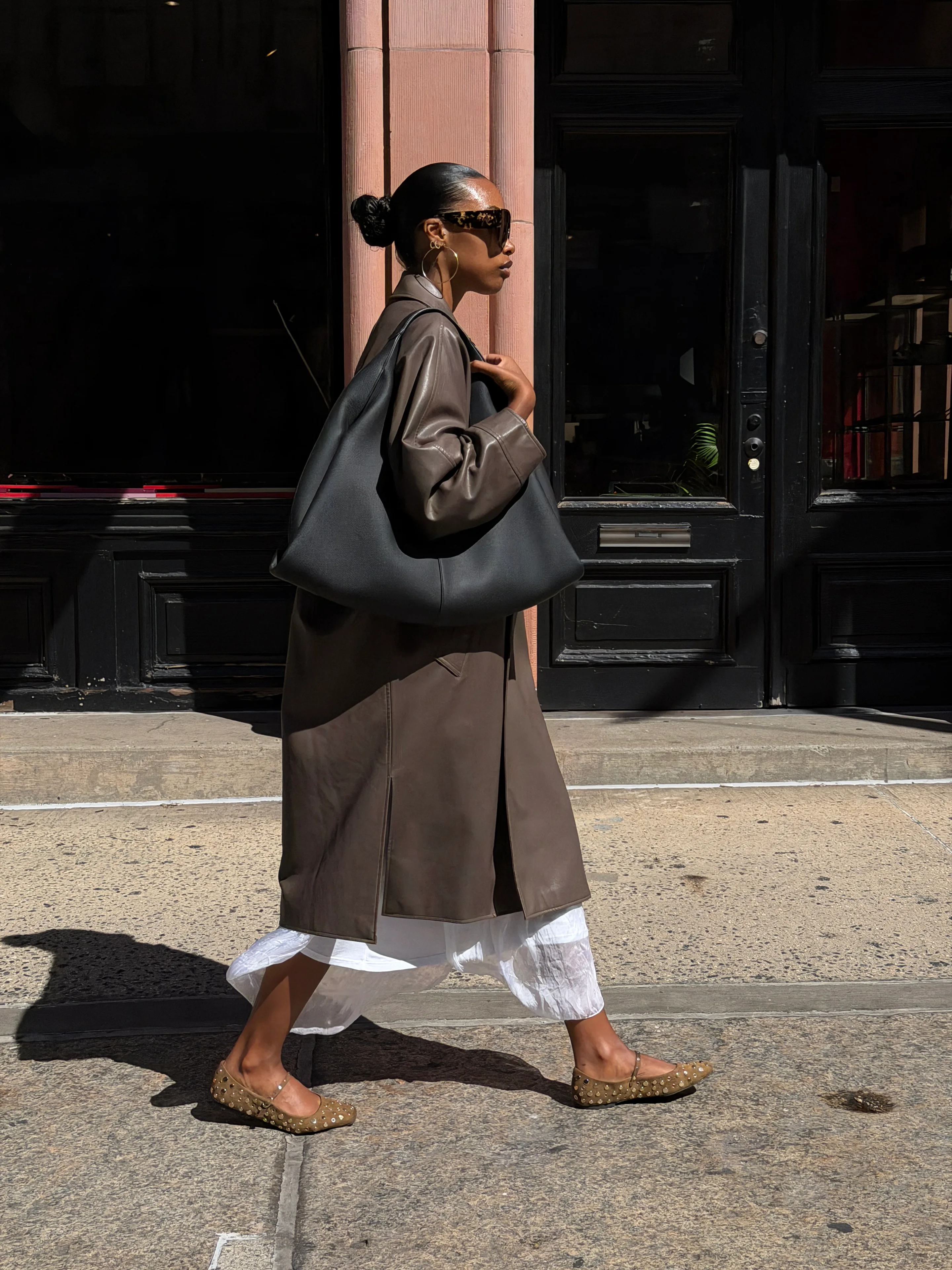 Brown leather trench coat, white dress, and studded flats with a large black bag.