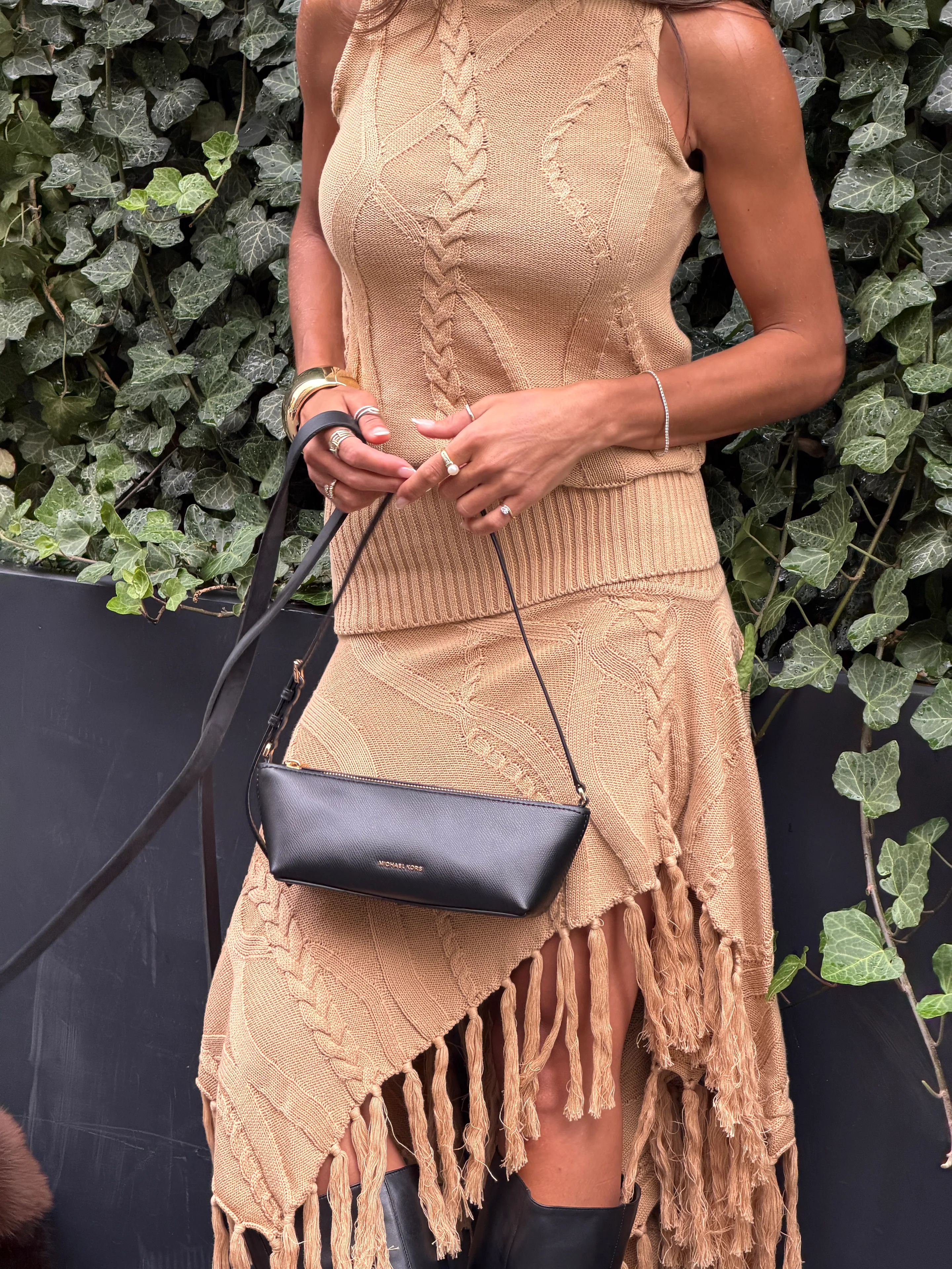 Beige knitted top and fringed skirt set with a black Michael Kors bag.
