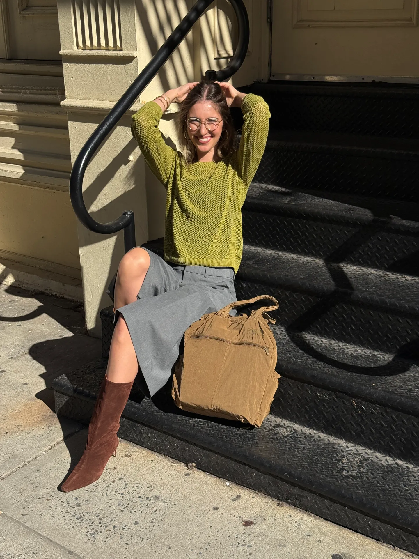 Lime green knit sweater, grey culottes, brown suede boots, and a tan bag on steps.