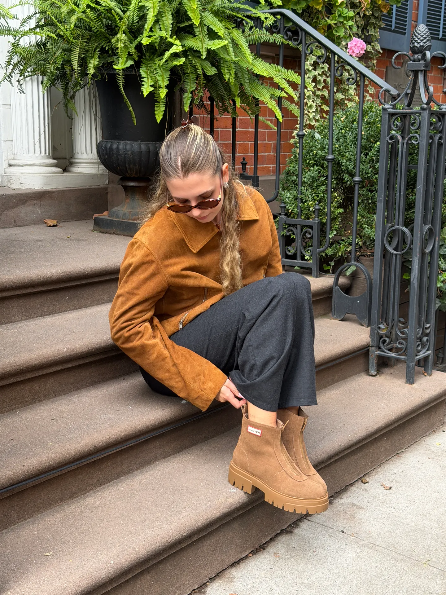 Brown suede bomber jacket, black wide-leg pants, and tan Hunter platform boots.