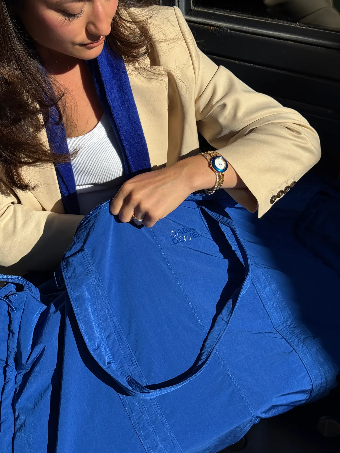 Beige blazer, white ribbed top, and blue scarf with a matching blue nylon bag.