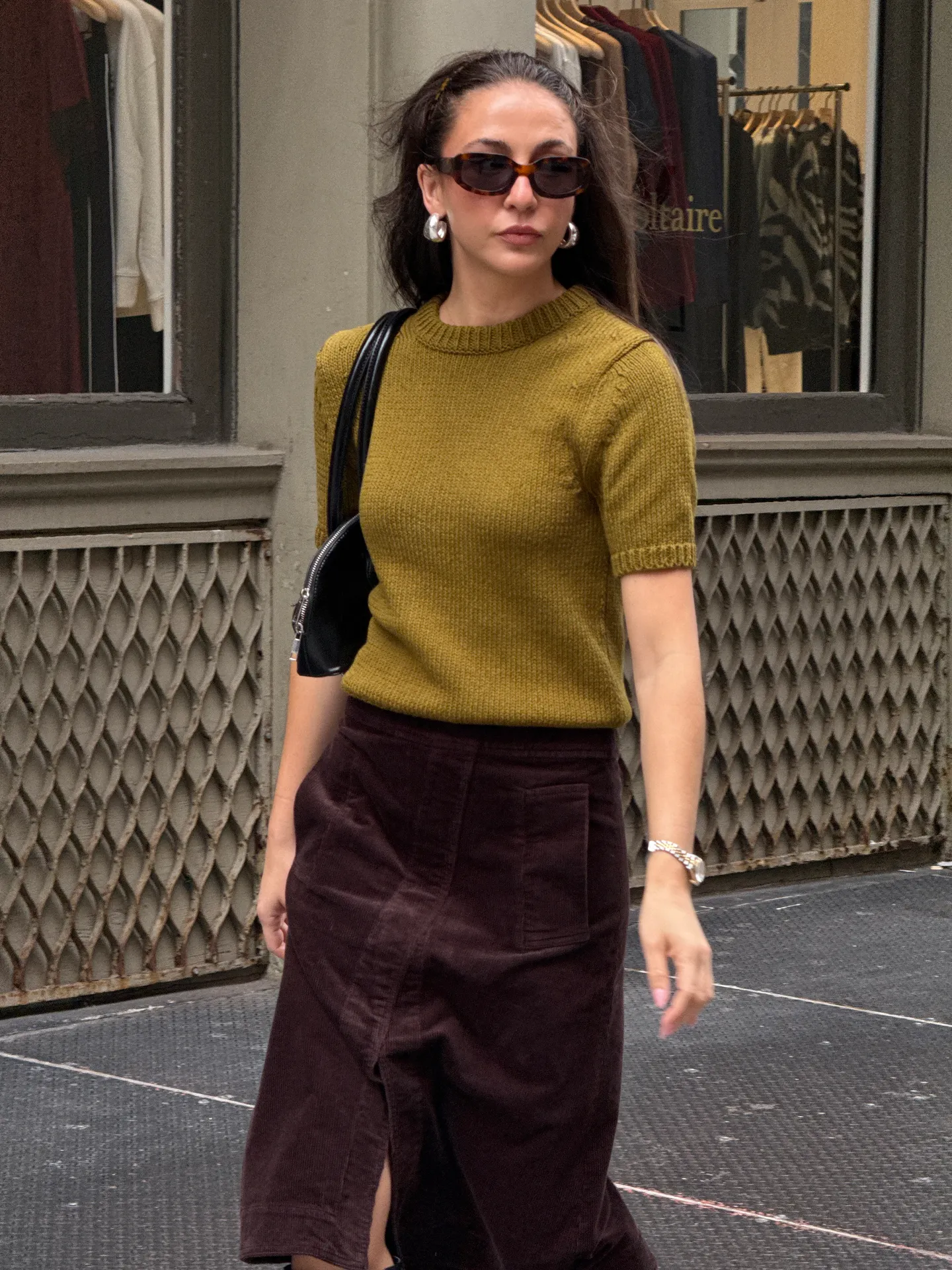 Olive green knit top, dark brown corduroy skirt, black shoulder bag, and sunglasses.