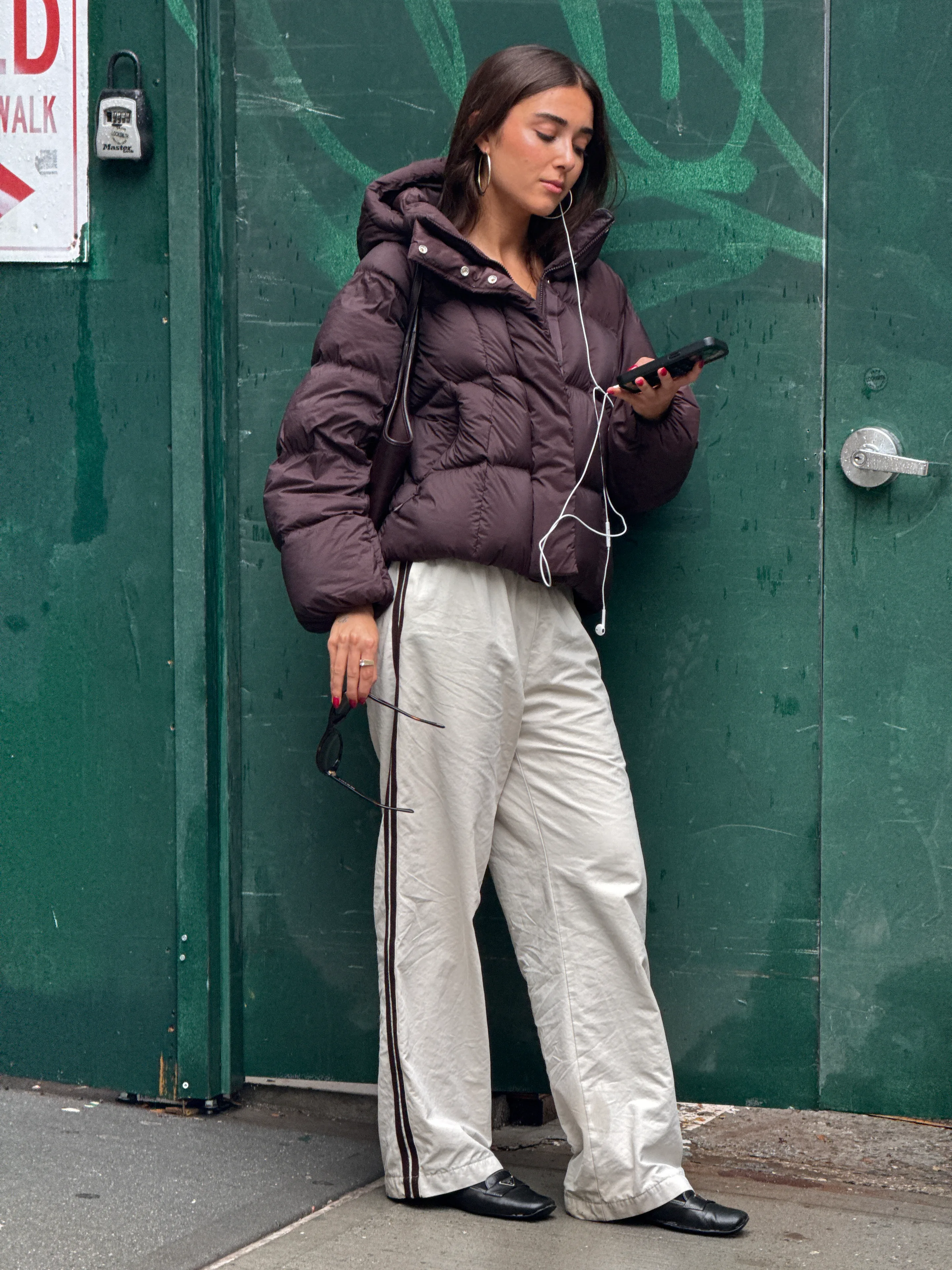 Brown puffer jacket, cream track pants, and black loafers on a city street.