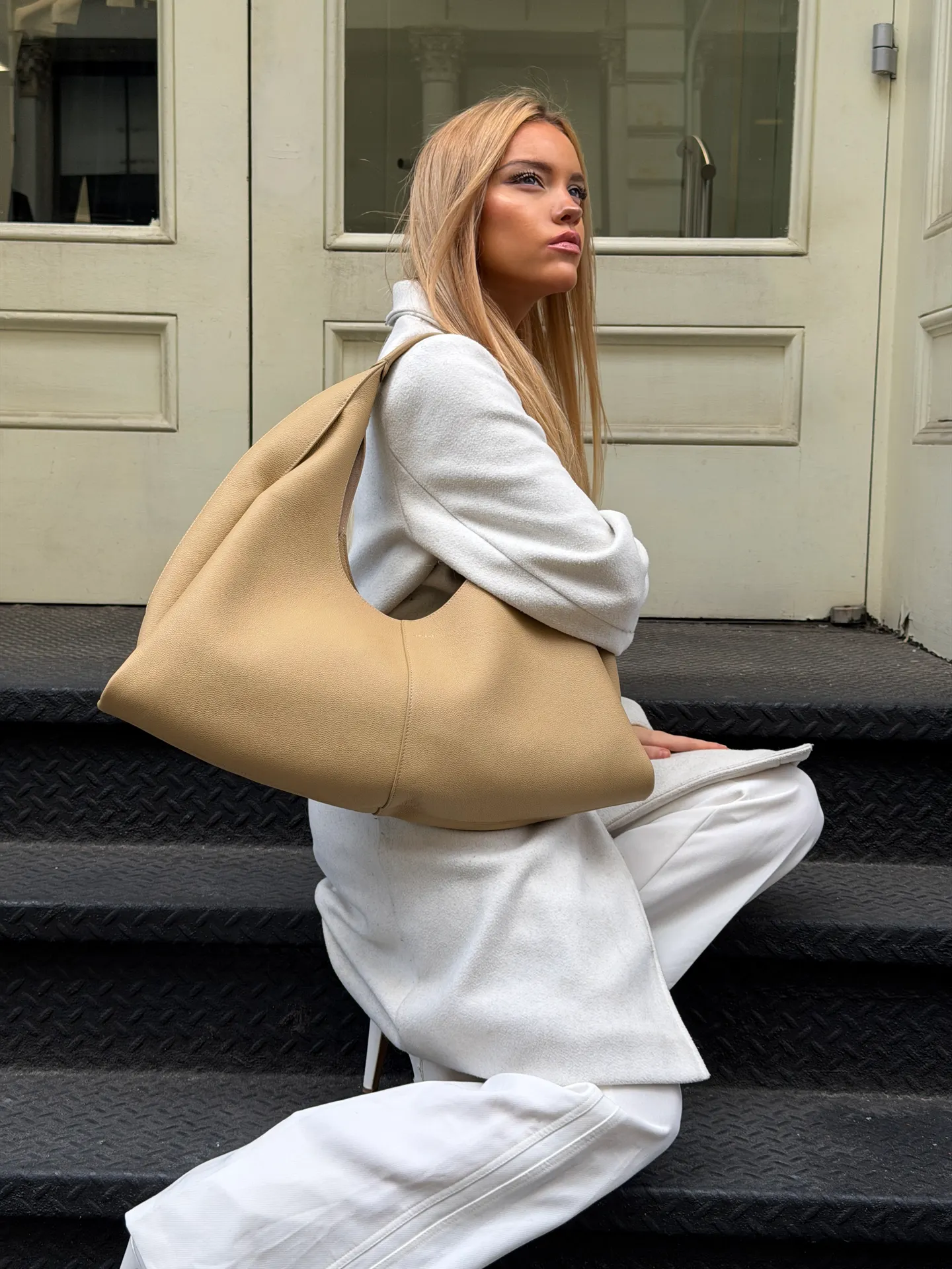 White long coat and pants paired with a large beige shoulder bag.