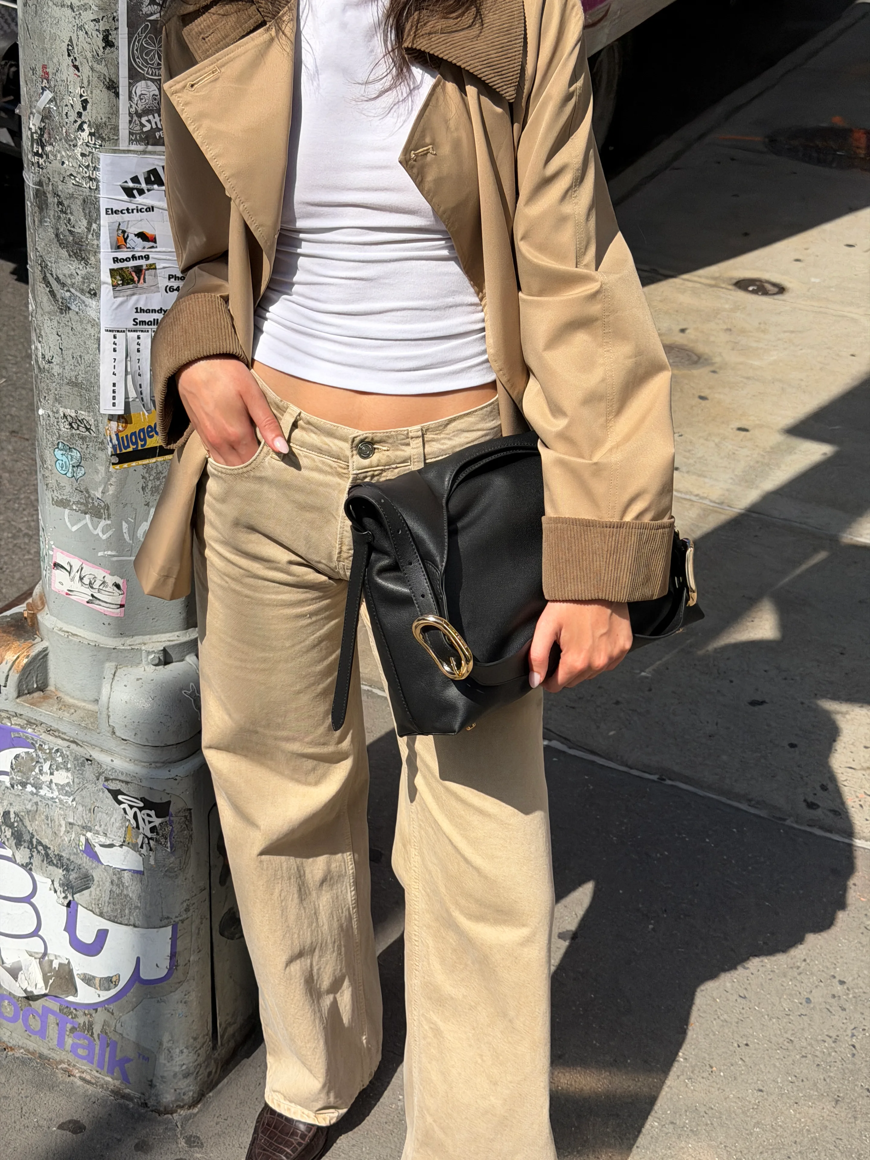 Tan trench coat over a white top, paired with beige wide-leg pants and a black handbag.