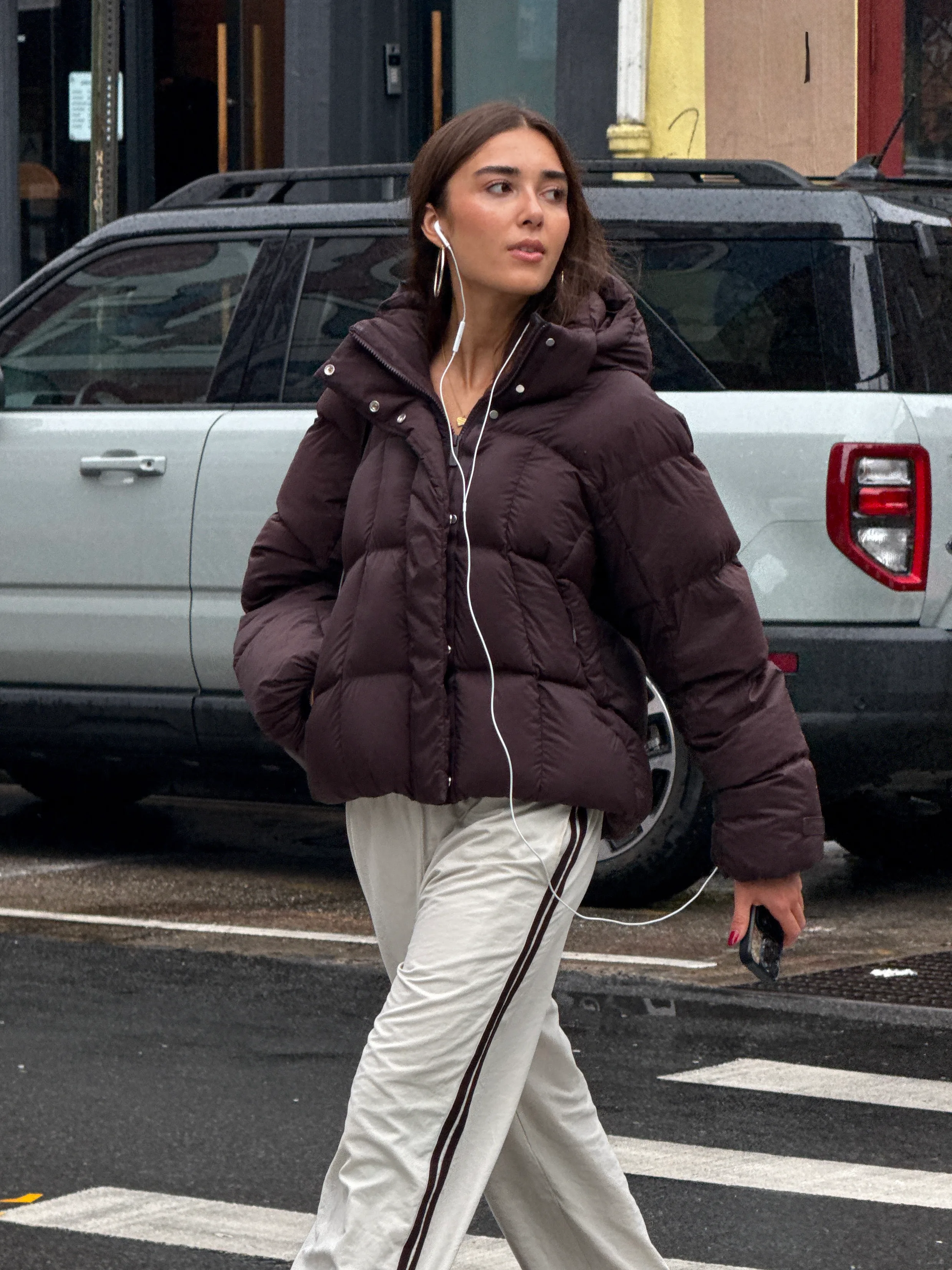 Brown puffer jacket, cream sweatpants, and silver hoop earrings on city street.