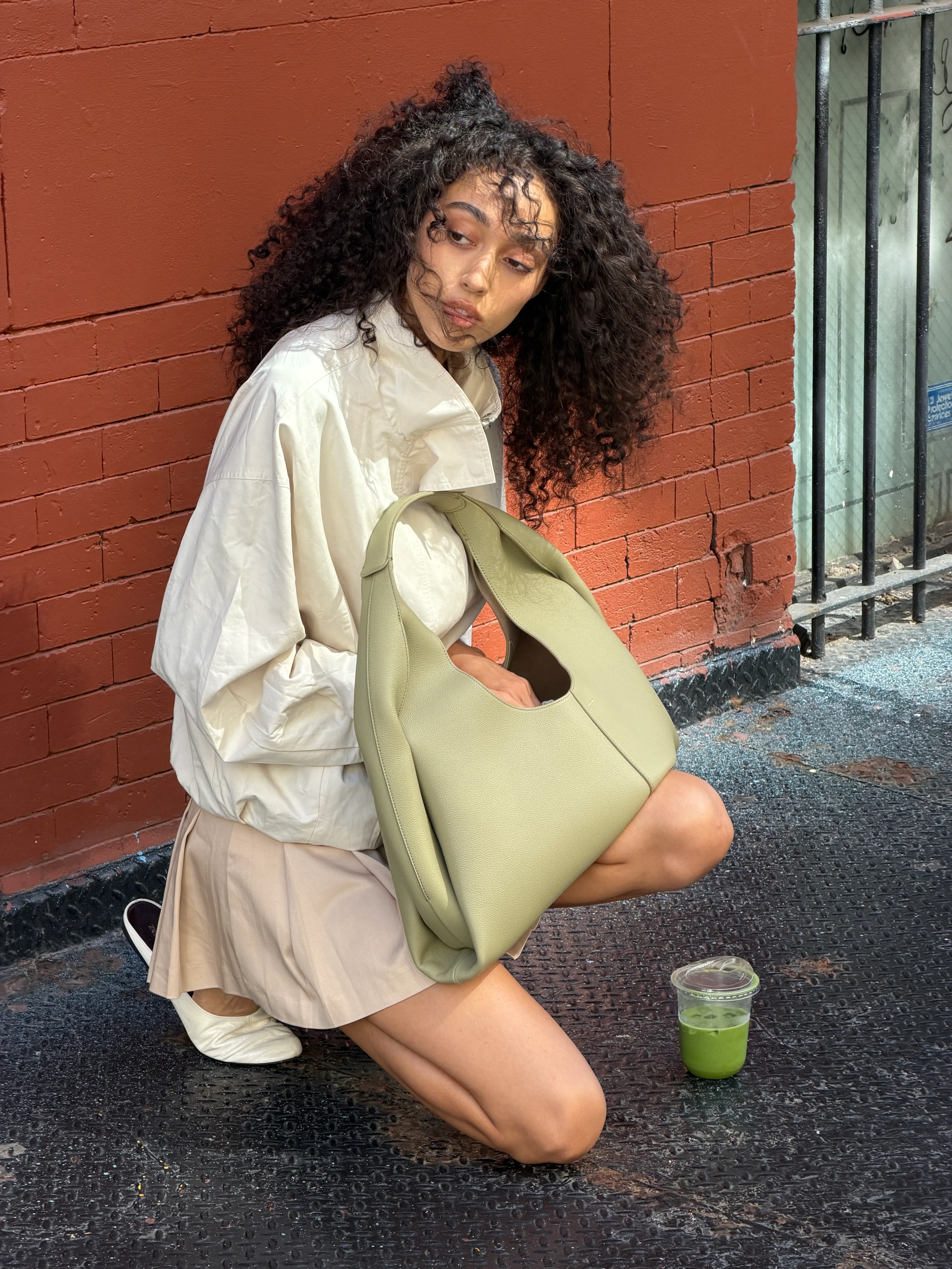 Off-white jacket, beige pleated mini skirt, olive green bag, and white flats.