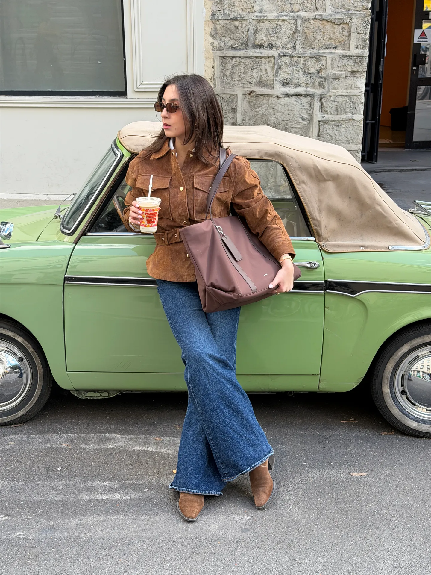 Brown suede jacket, flared jeans, brown tote bag, and boots by a green vintage car.