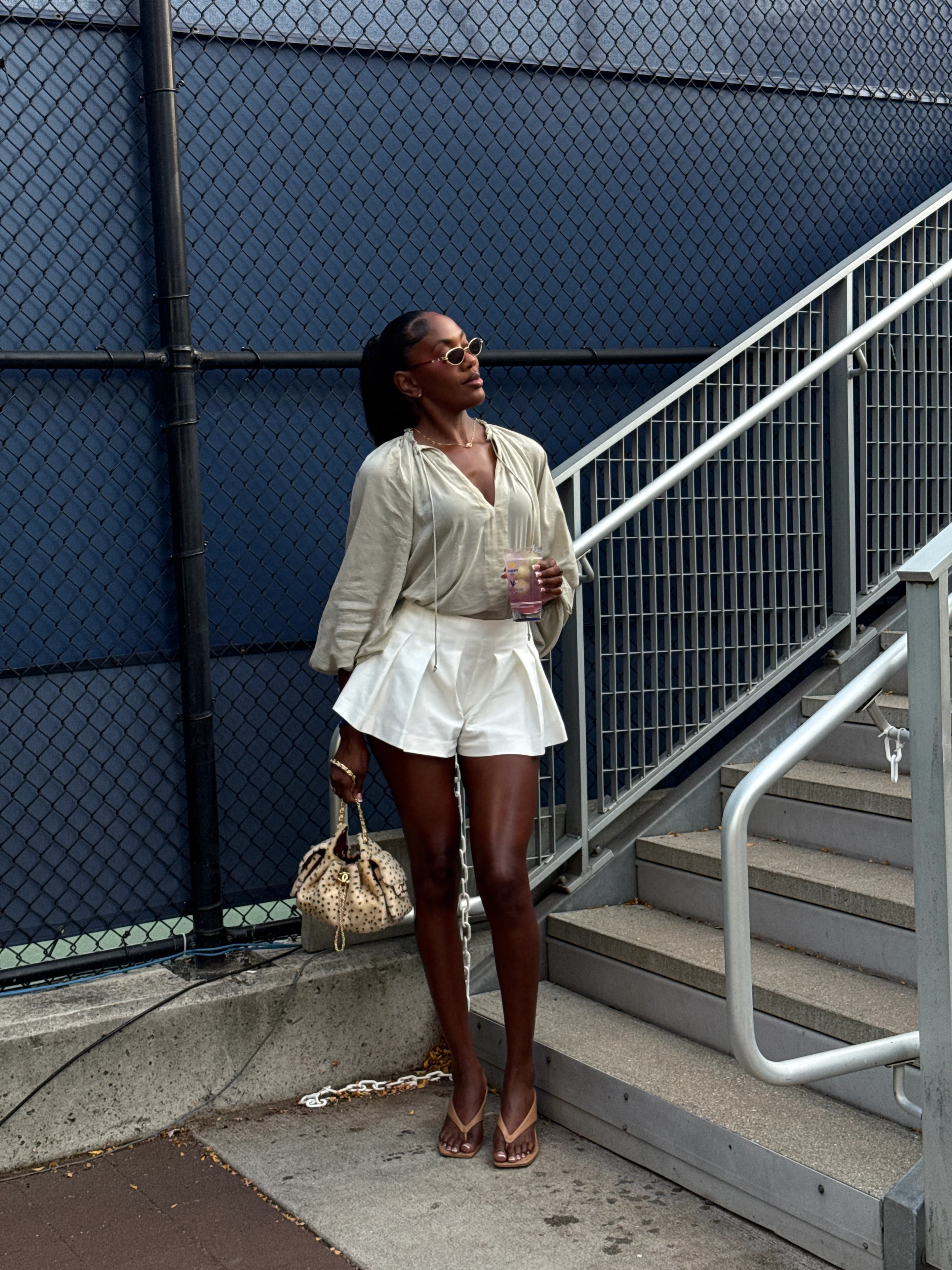 Neutral linen blouse, white pleated shorts, beige mules, and a leopard print handbag.