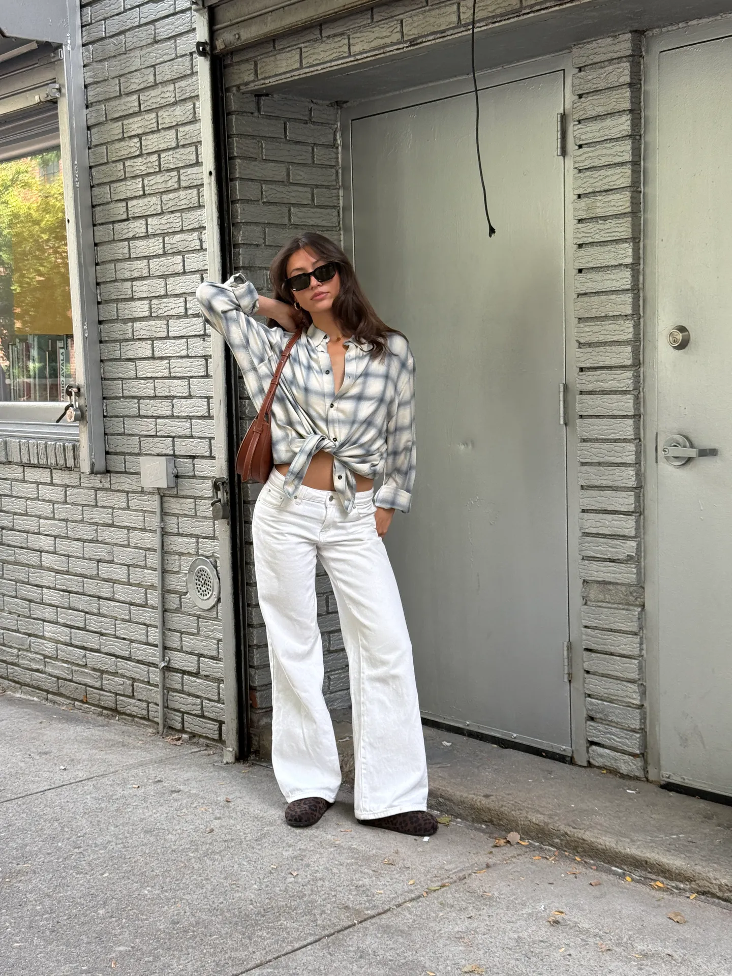 Blue and white plaid button-down shirt tied at waist, white wide-leg jeans, brown bag, sunglasses.