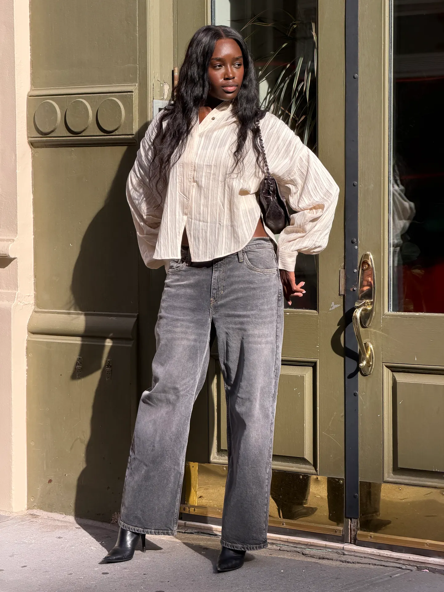 Beige striped button-up shirt, gray wide-leg jeans, black heeled boots, and black shoulder bag.