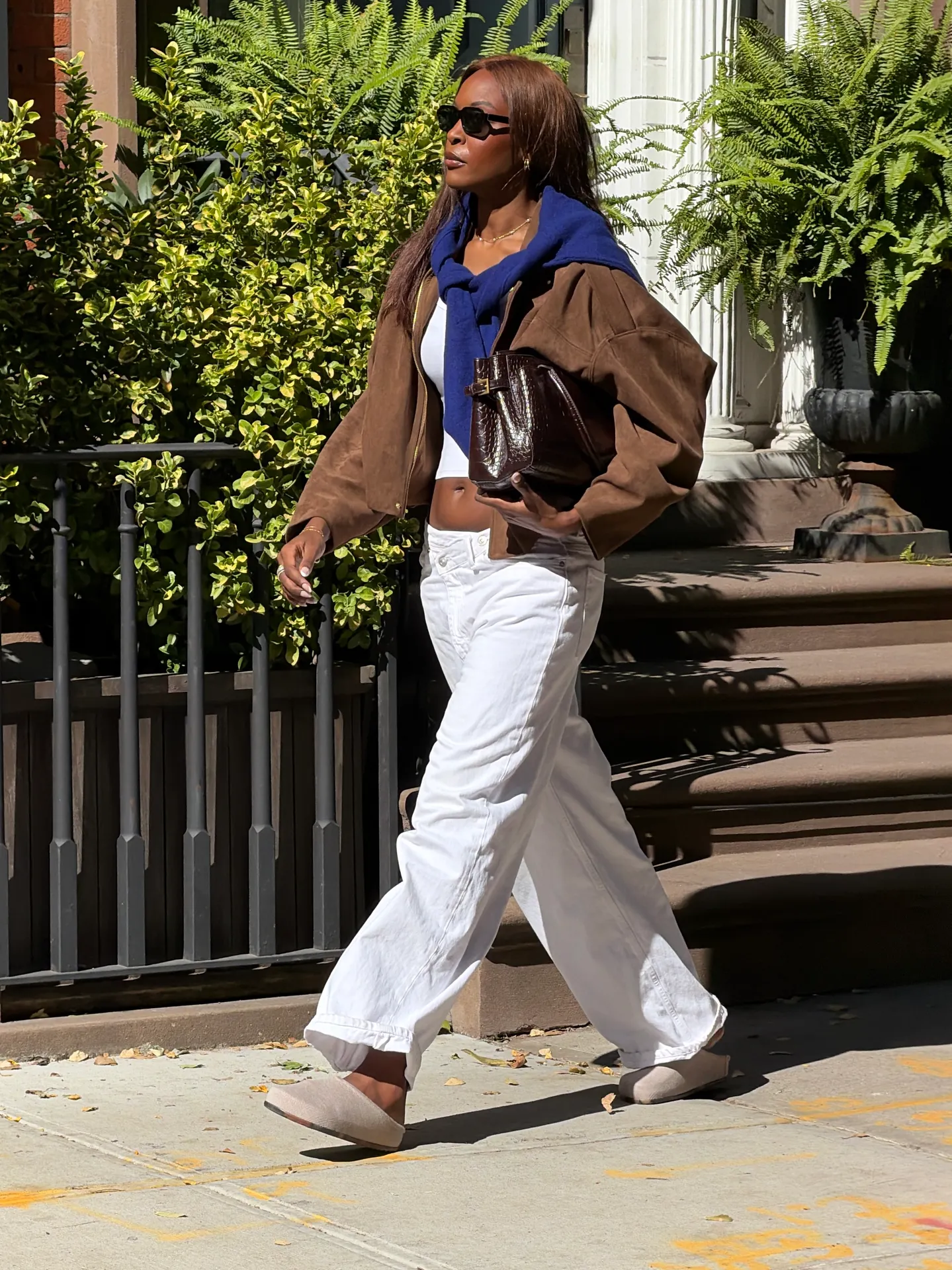 Brown bomber jacket, blue sweater, white crop top, white baggy pants, and beige clogs.